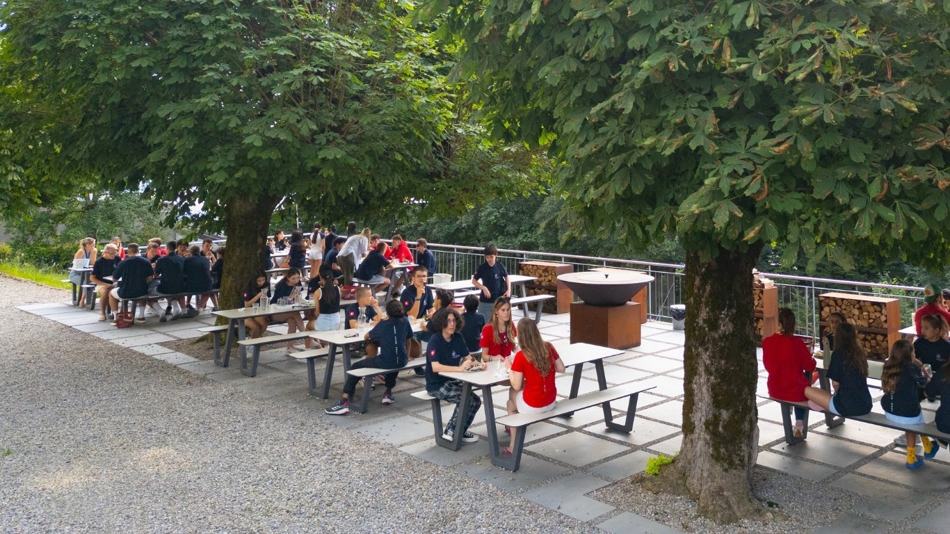 A group of students enjoy their meals at an outdoor eating area surrounded with trees.