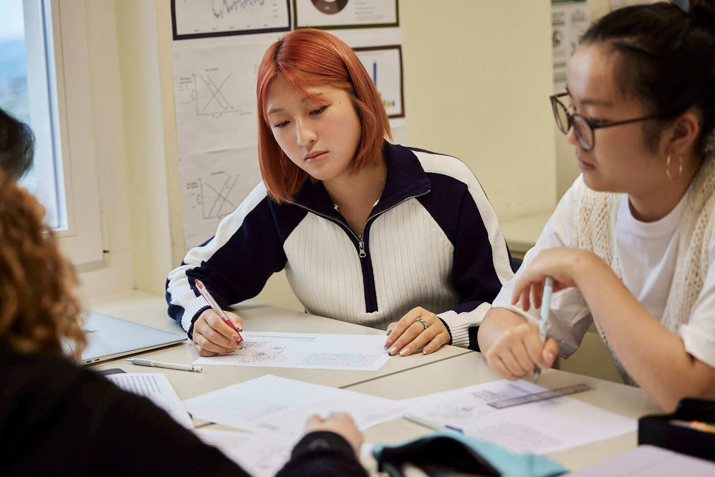 Two female students in sit next to each other in a class discussing some assignments.