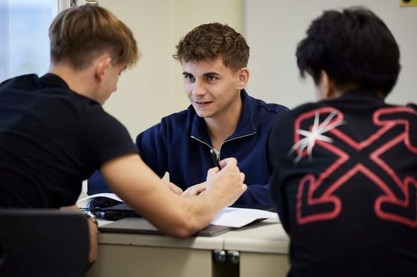 Three male students sitting in a class discussing something.