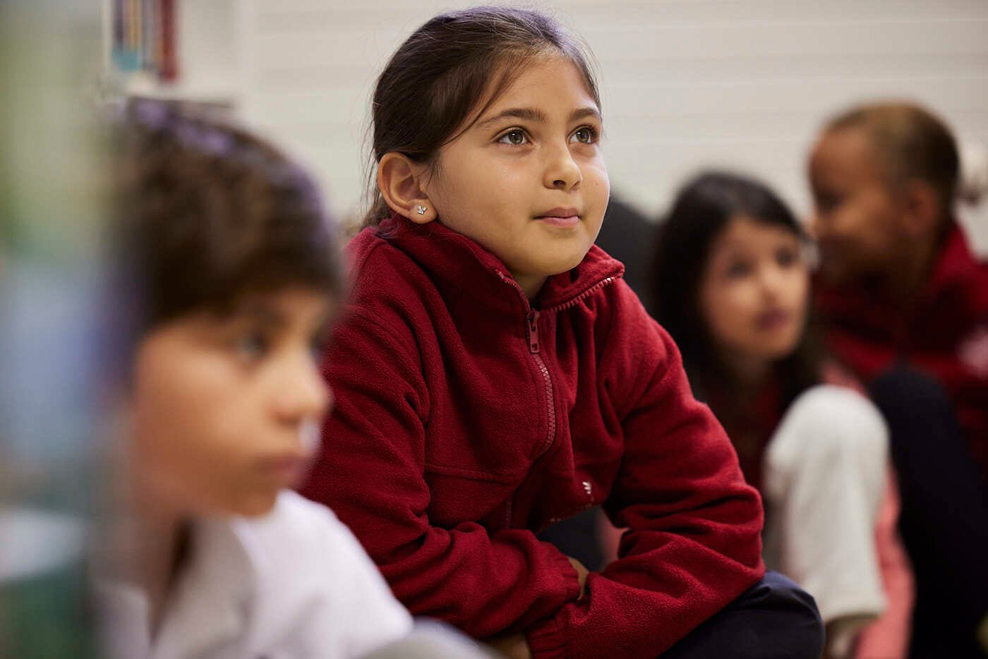 A girl student listens to someone in a class, she is wearing red sweater.