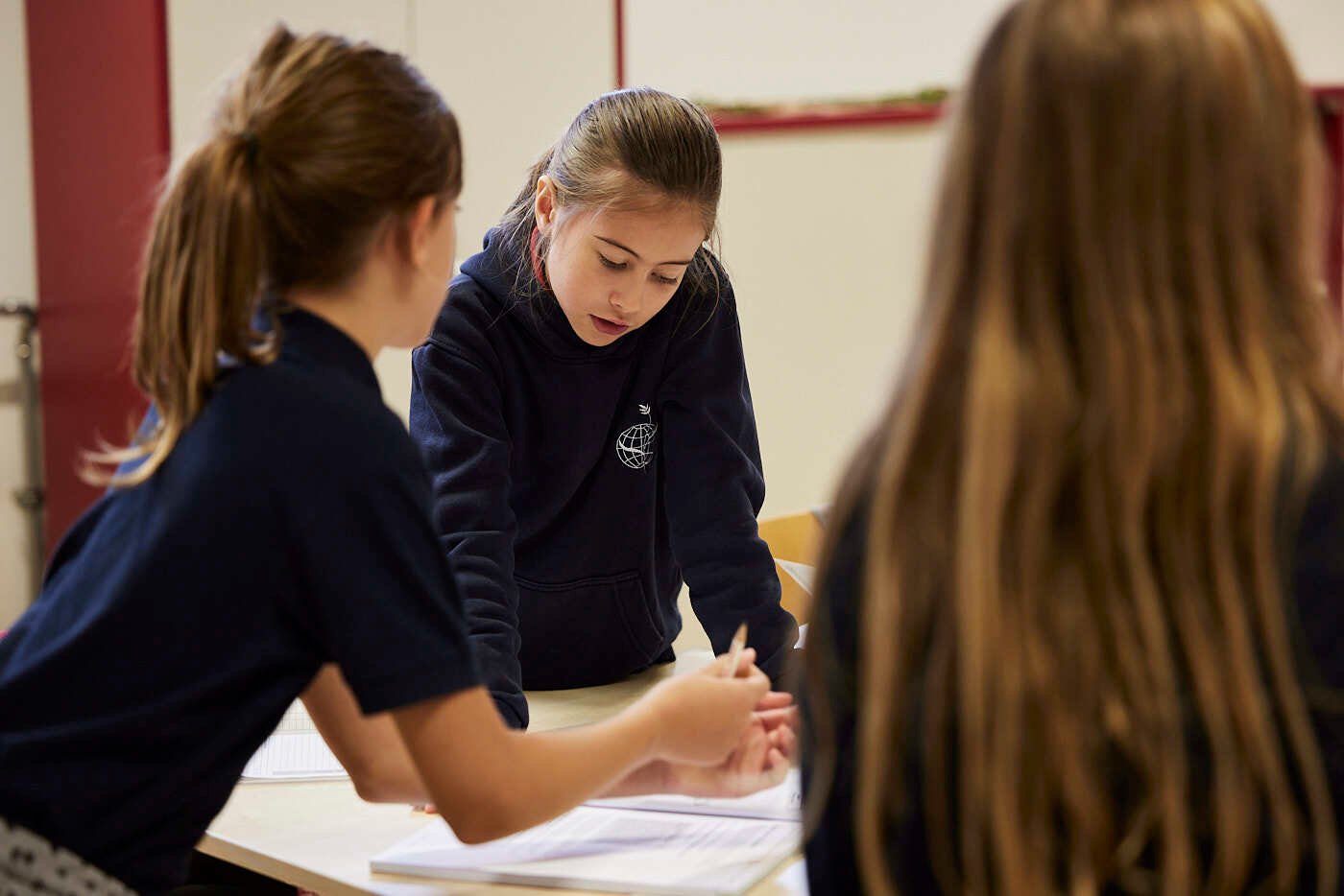 Three girl students discuss something in a class.