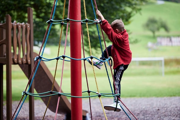 A boy student climb a rope play on a field.