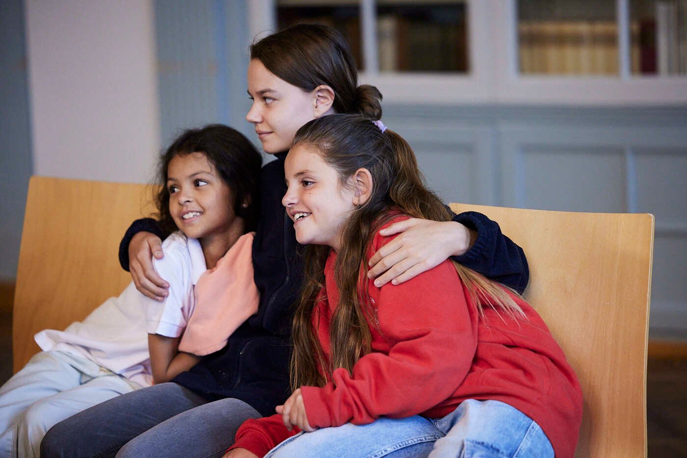 three young girls cuddled on a yellow sofa.