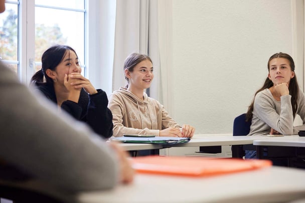 Three female students sit down in a class, each gives a different expression.