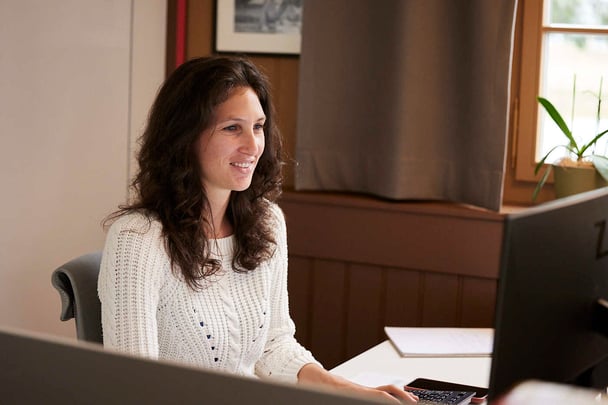 Frau mit weißem Oberteil schaut lächelnd auf ihren Computer.