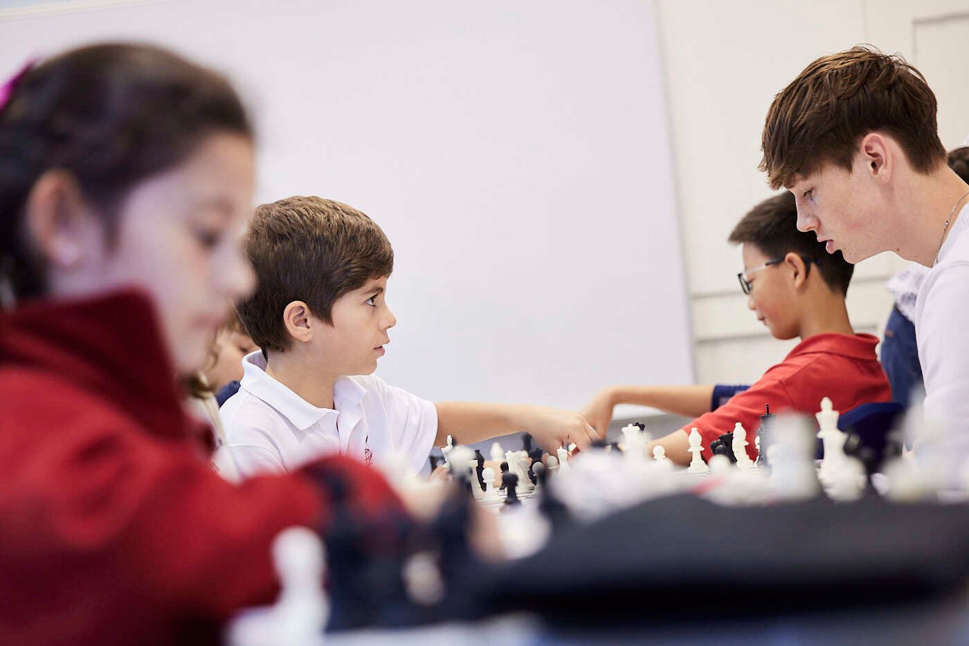 Several young students and a male mentor play chess.