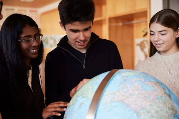 Two girl students and a boy student observing and learning a globe.