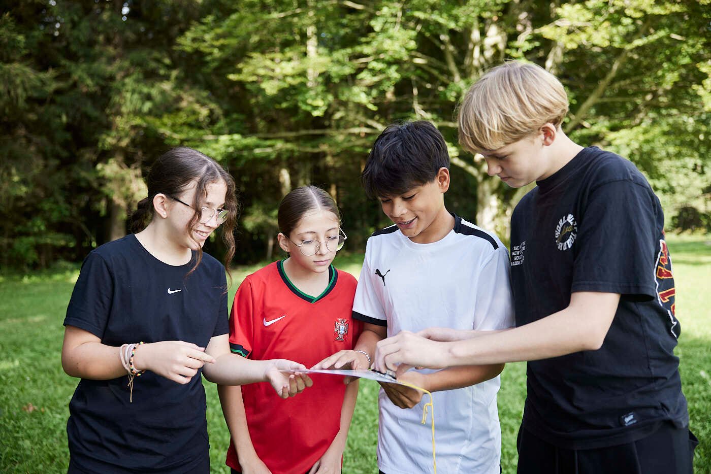 Two girl and two boy students gathering on a field, looking at an instruction paper.