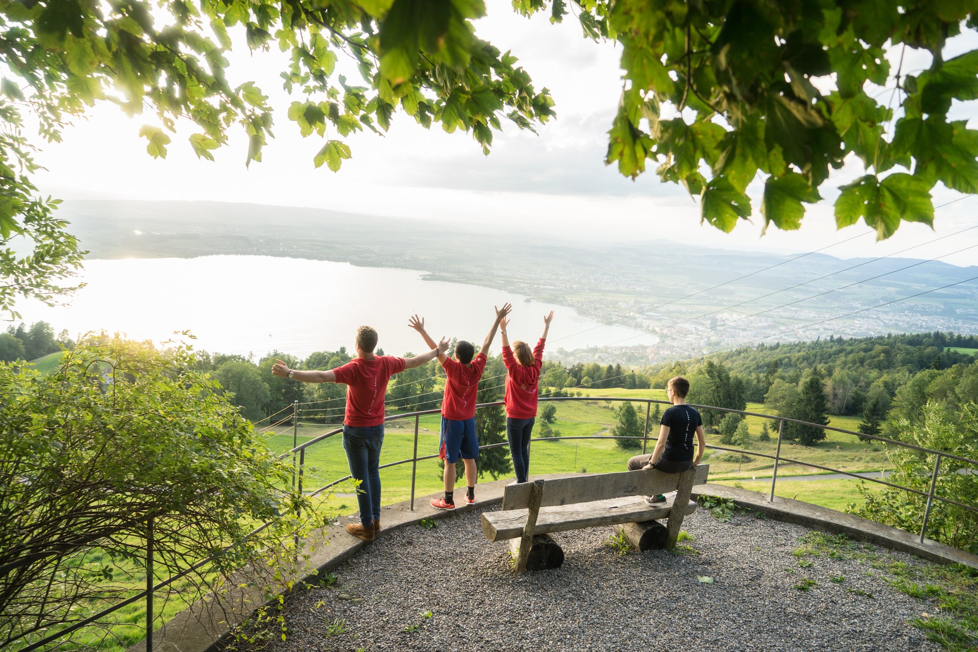 Three young men in front of a lake view raise their hands. 