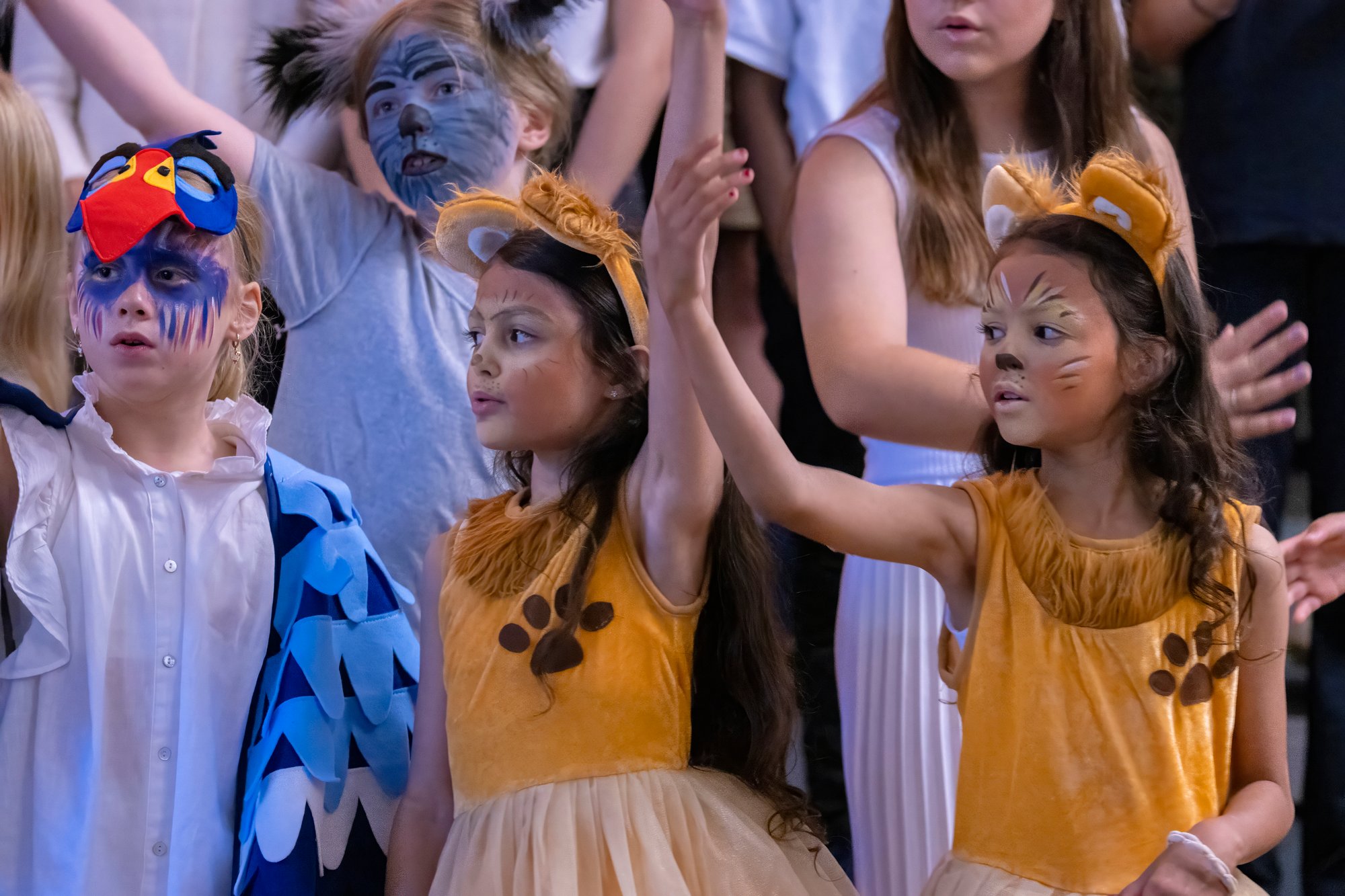 A group of children perform a play with three girls in the front being a focus.