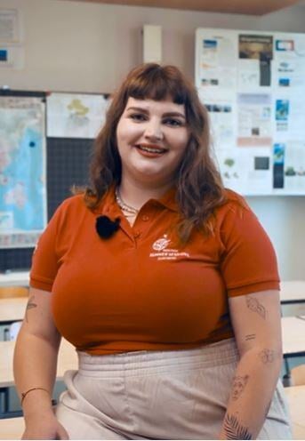 A young female mentor in a class talks to camera. 