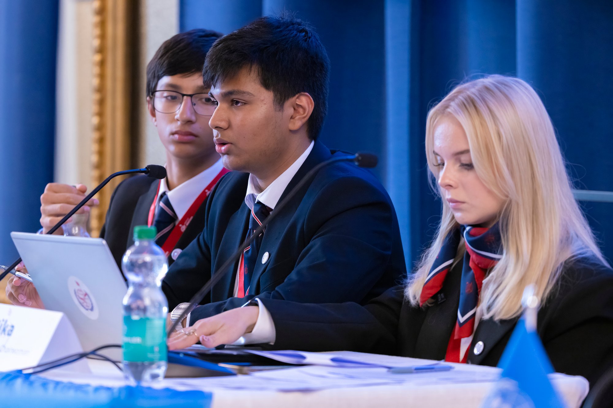 Two male students and a female student sit at chair of model united nations conference.