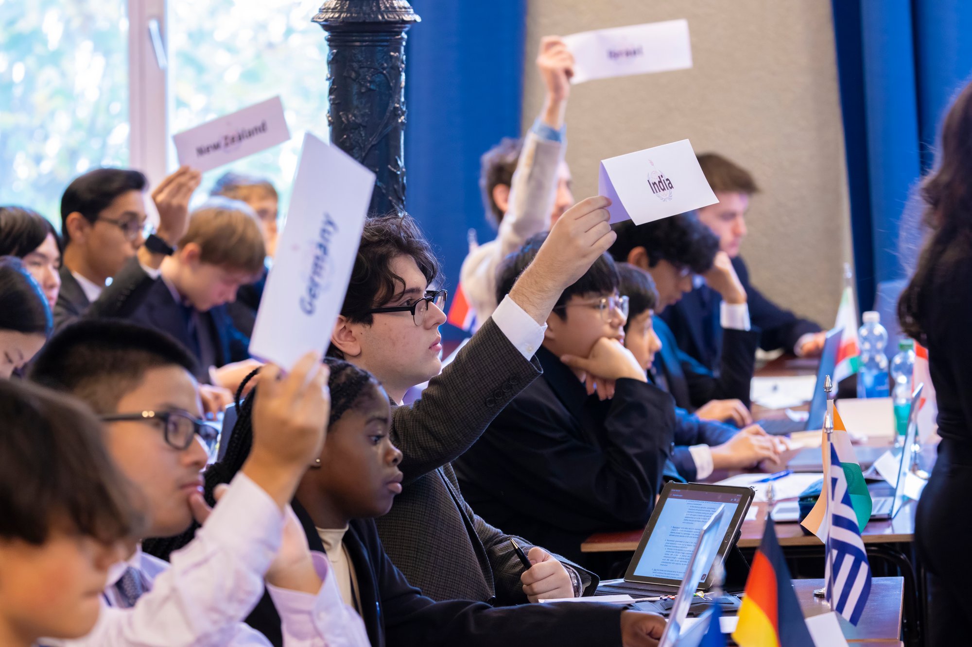 A group of students raising their country delegations name signs at model united nations conference.