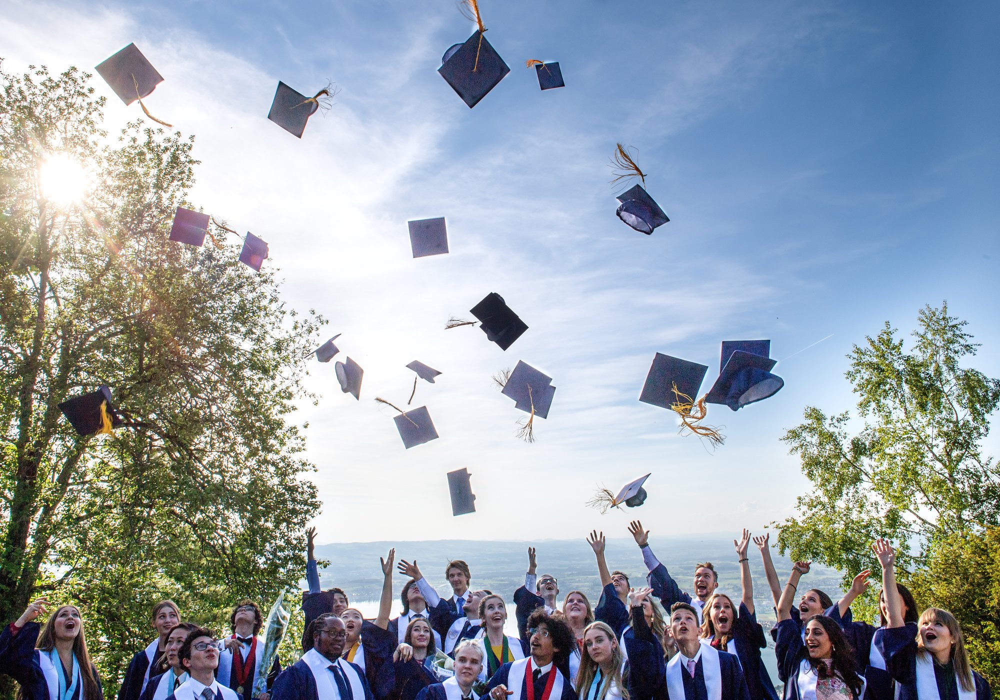 A group of students dressed in their graduation outfits throw away their graduation caps.