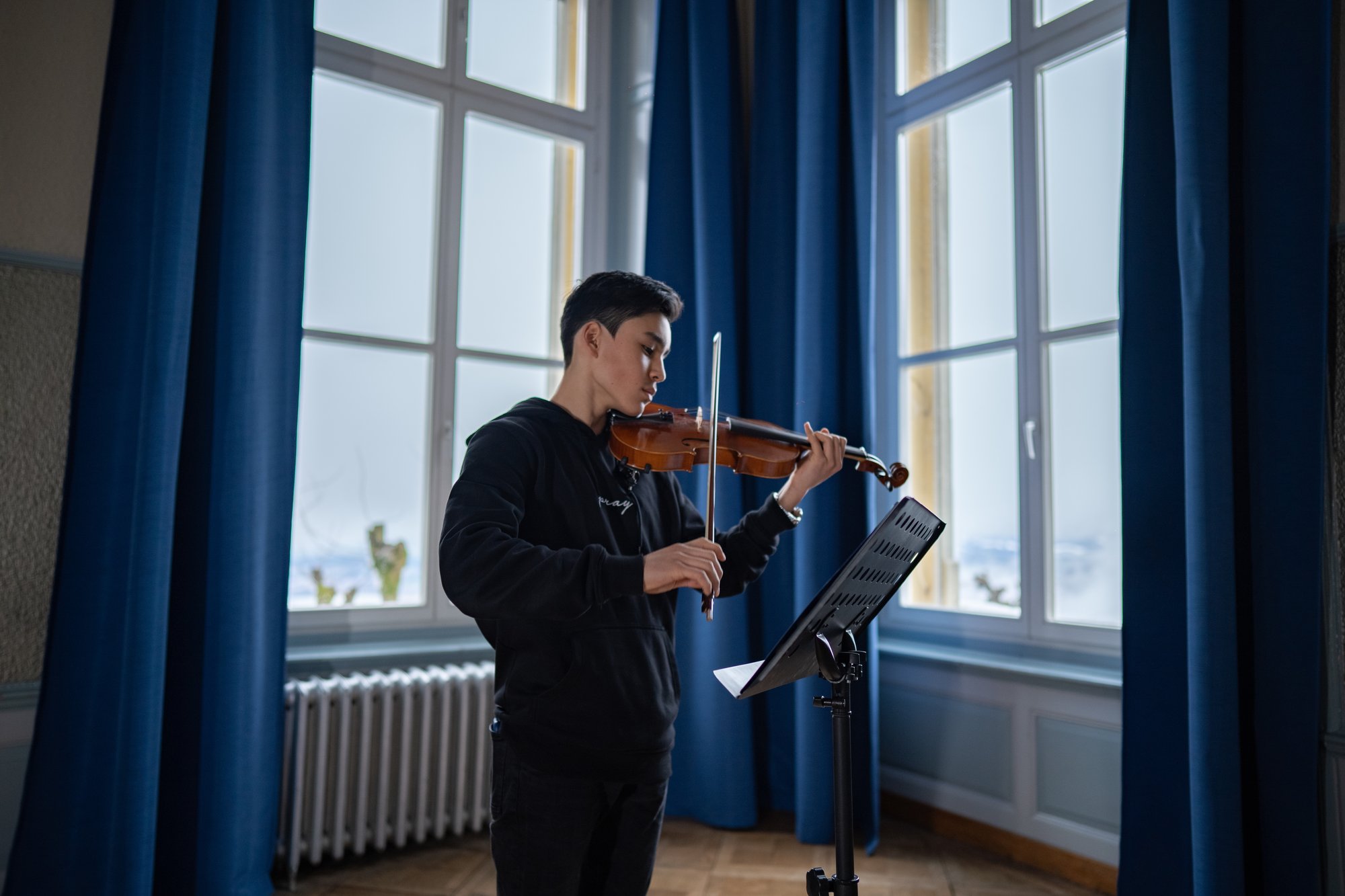 Ein Schüler spielt Geige in der Mitte einer Aula.