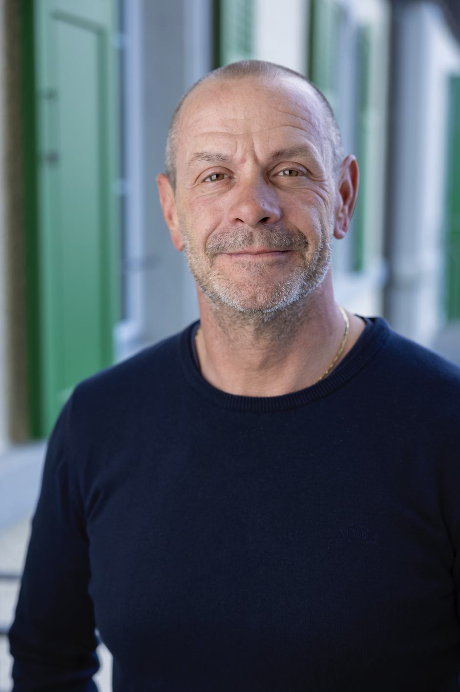 A male staff with dark blue top smiles at camera.