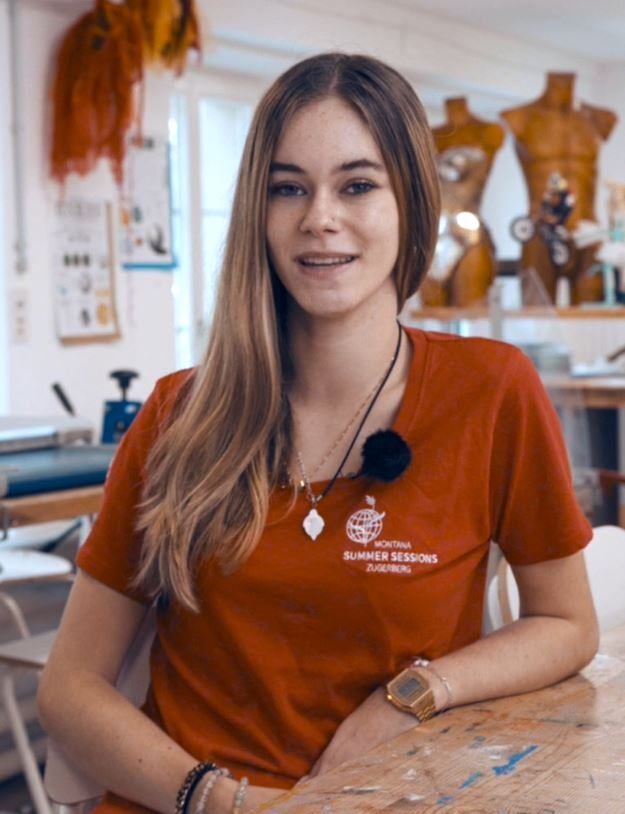 A long-haired young female mentor in an art lab and talks to camera. She wears a red top written Montana Summer Sessions.