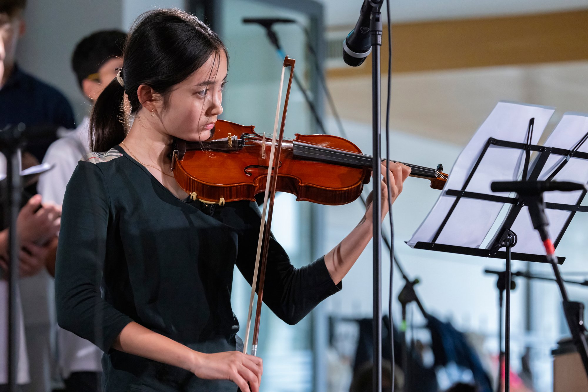 A girl in black outfit plays a violin in a concert room.