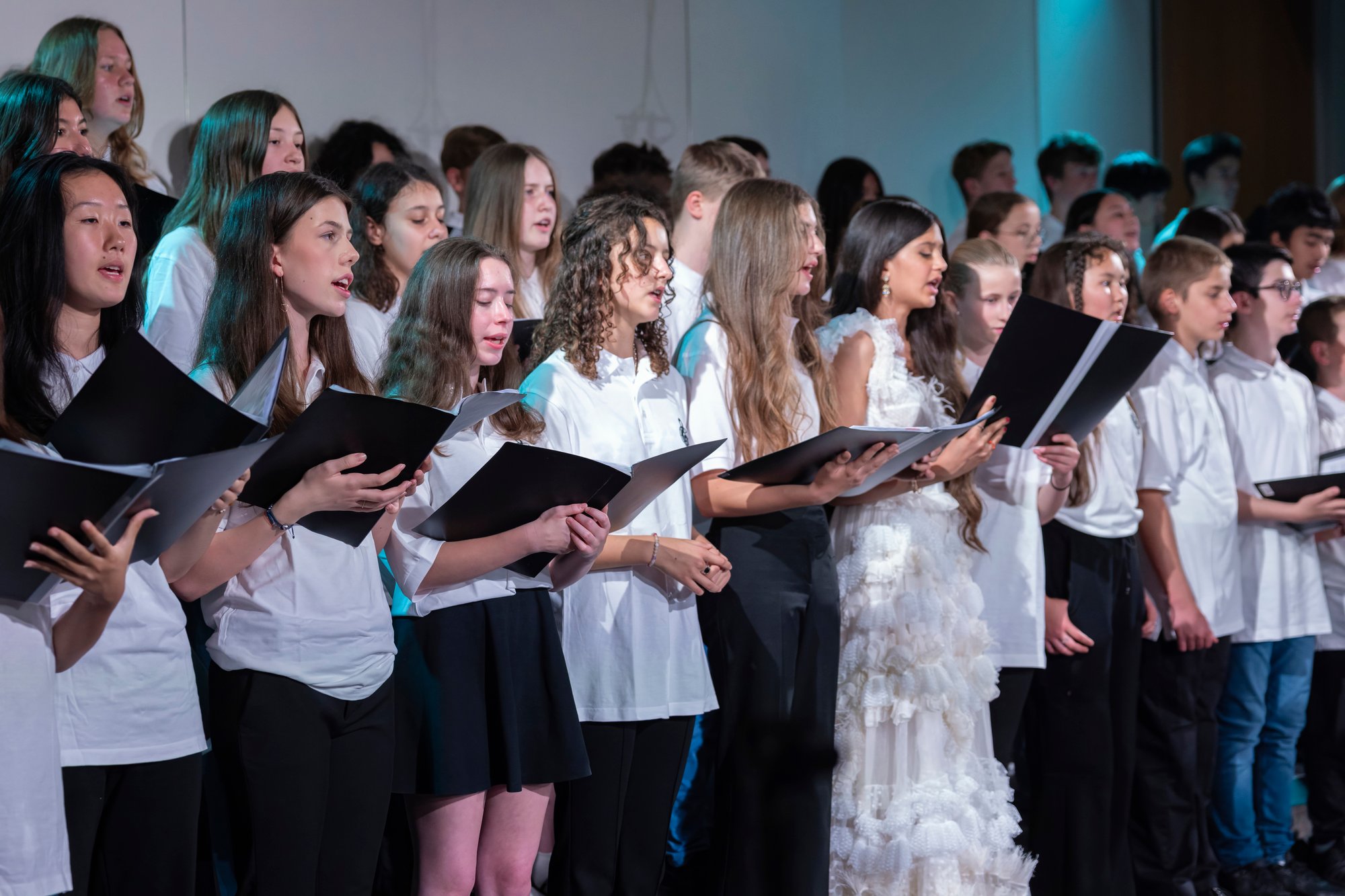 A group of choir students in white outfit sing.