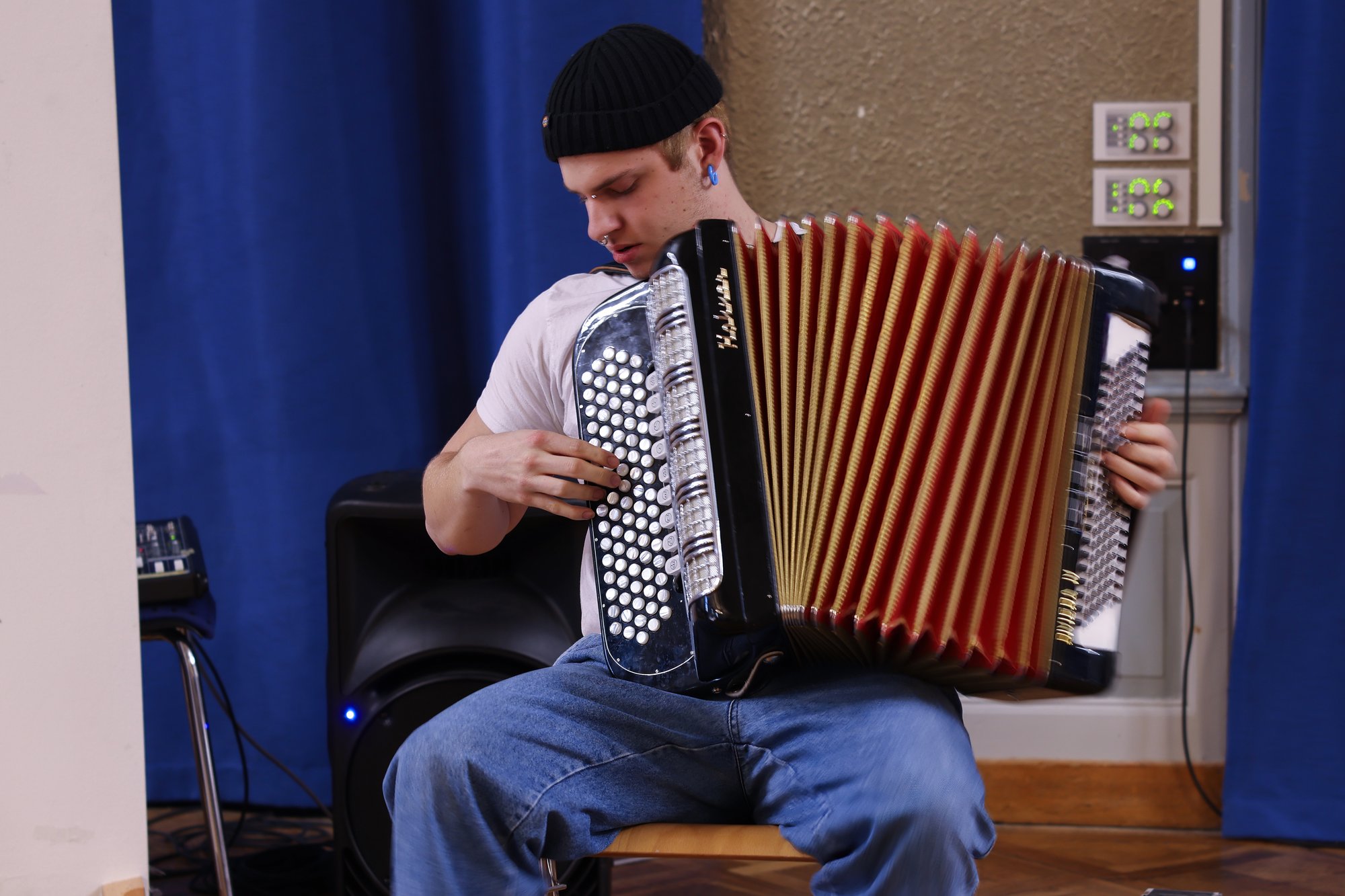 A young man sits in a room and plays accordion.