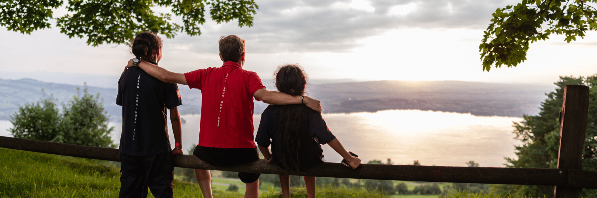 Two boy students and a young male mentor enjoy the Zug sunset view on a summer day.