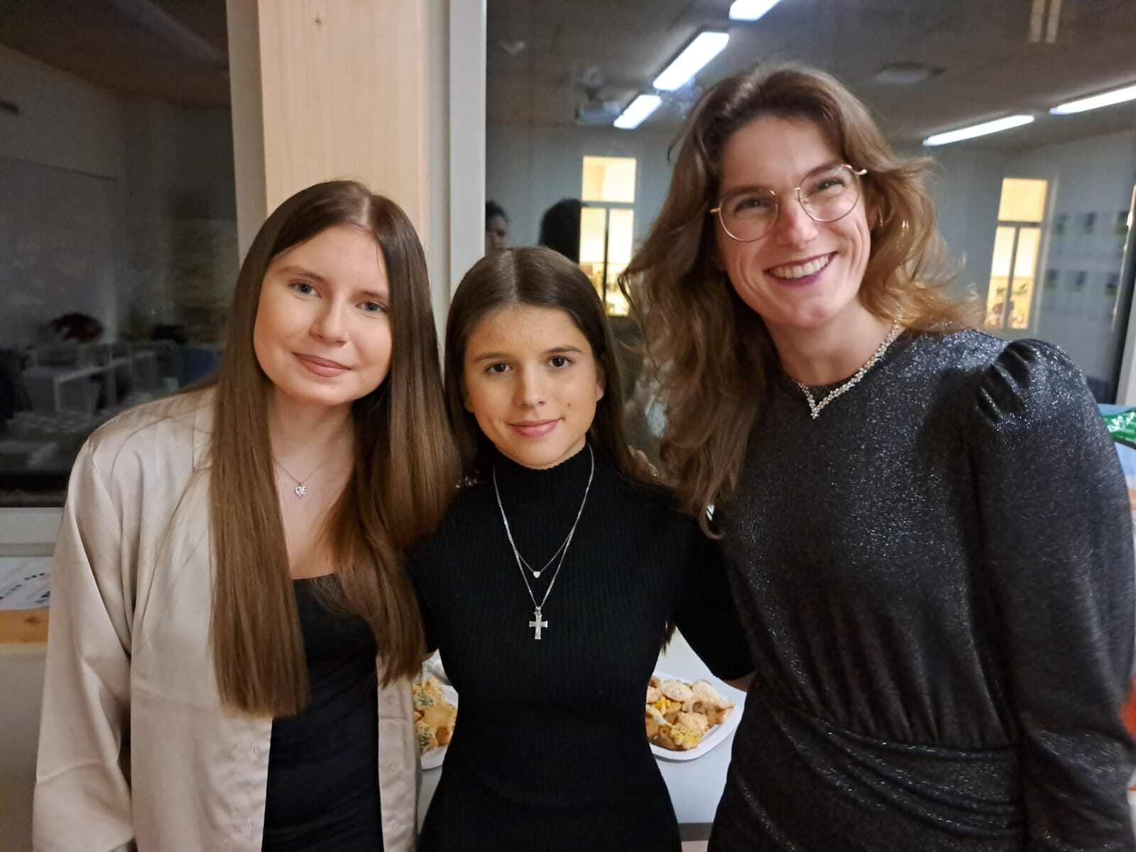 Two girl students and a teacher pose and smile to camera.