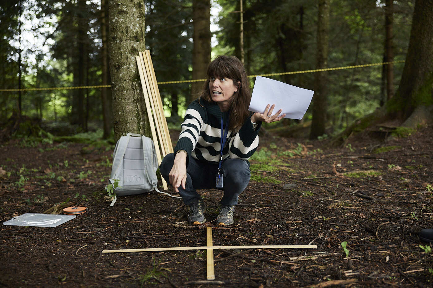 A woman squatting in a forest who giving instructions.