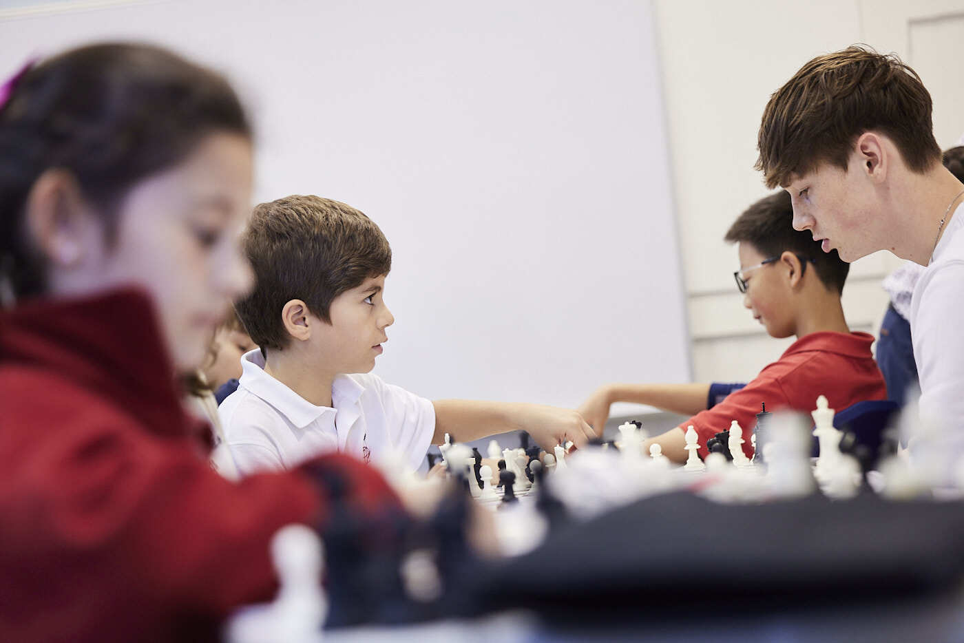 Mehrere junge Schüler und ein Mentor spielen Schach