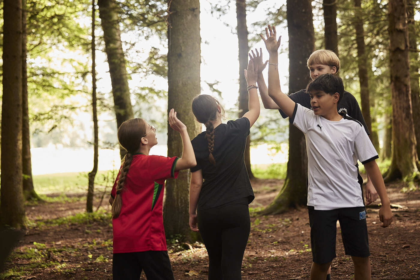 Two girl students give high-five to two boy students in a forest.